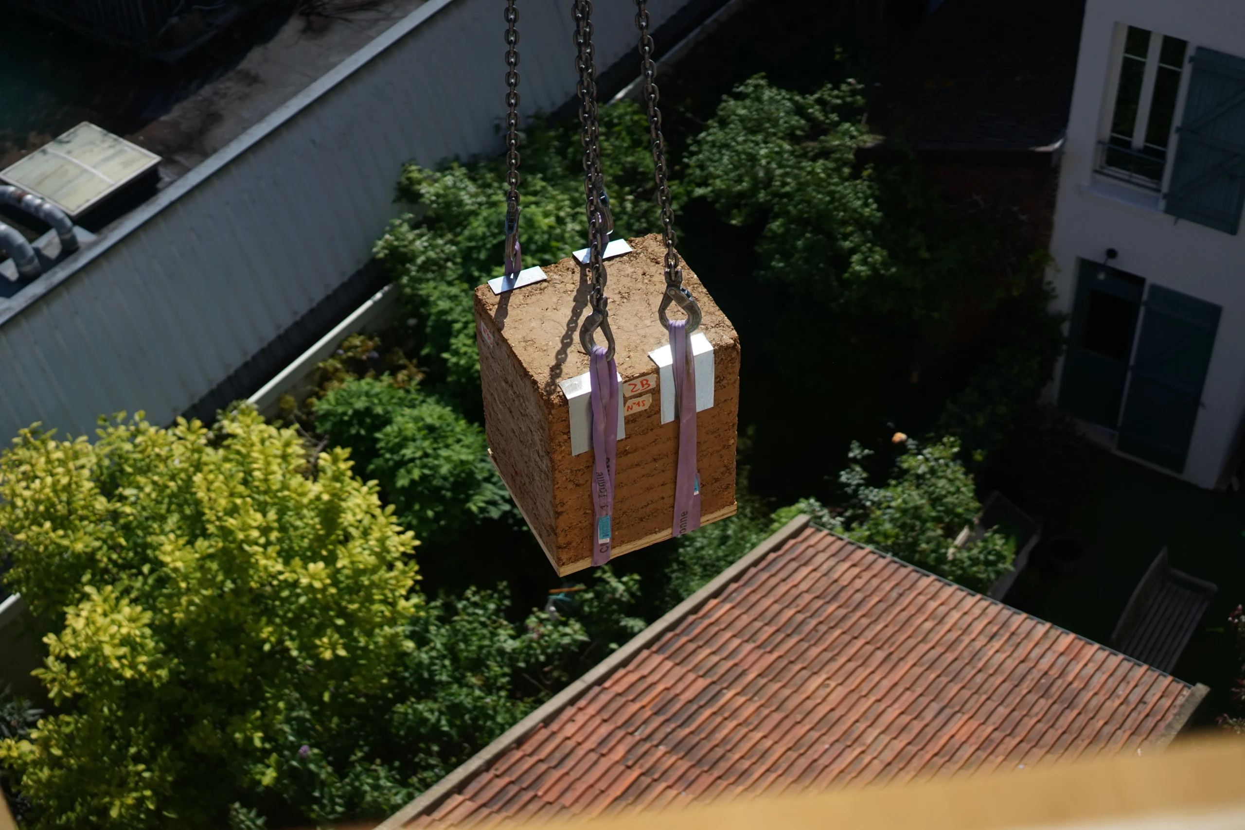 Bloc de pisé préfabriqué en terre crue suspendu à une grue